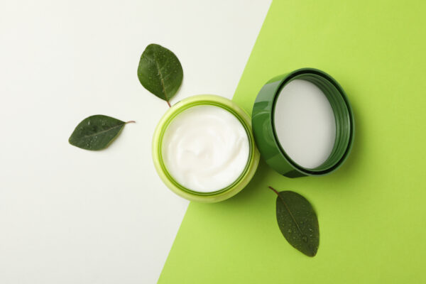 jar of cosmetic cream and leaves on two tone background