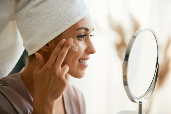 beautiful woman applies face cream while looking herself in mirror.