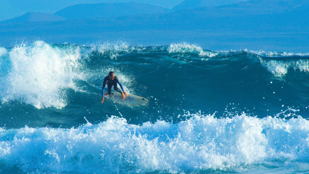 big barrel wave pushes the young surfer towards the coastline of canary islands.