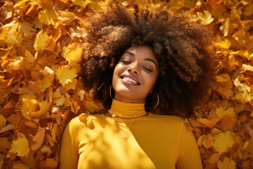 beautiful black woman smiling in autumn leaves, fashionable portrait in fall season, orange autumn tones