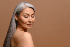 headshot of attractive middle aged asian woman with naked shoulders and long silver hair