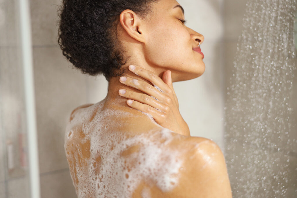 a woman lathers soap on her shoulder while taking a shower