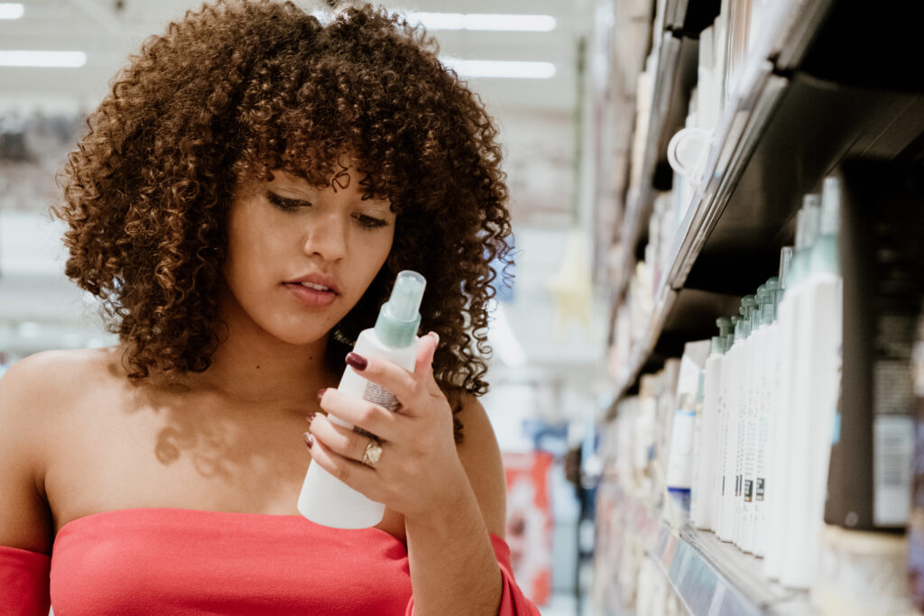 happy young brunette with curly hair buying shampoo in supermarket