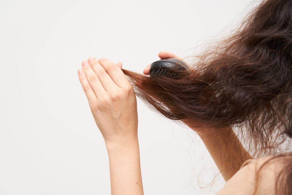 woman brush her dry and frizzy natural curly hair that needs hydration. natural curls before salon treatment. close up.